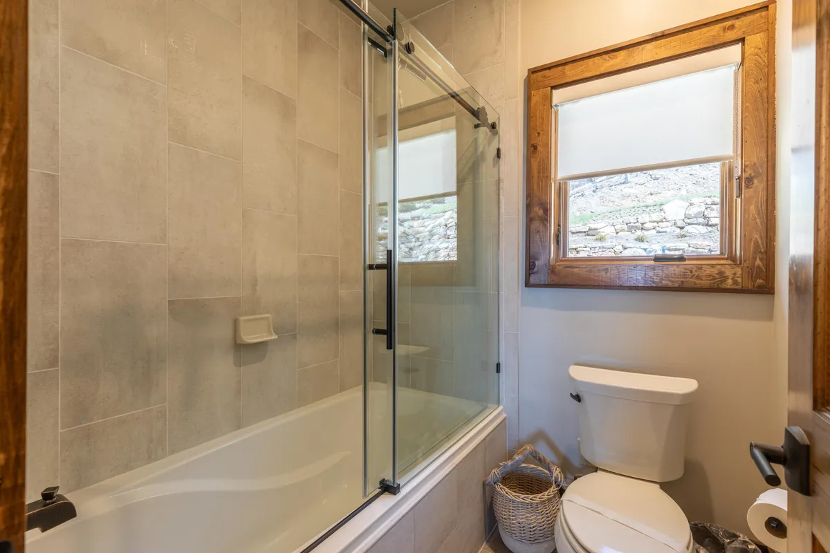 A calming en-suite bathroom featuring a standalone bathtub next to a window with a wooden frame and a glass-enclosed shower. The space is designed for relaxation, with soft natural light and a tranquil mood ideal for soothing baths after a day’s adventures.