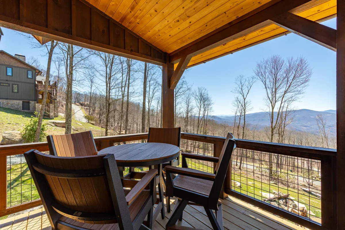 A serene patio with wooden furniture overlooks sweeping mountain views and a lush, natural landscape. The setting is perfect for a quiet morning coffee, reading a book, or simply taking in the sunrise or sunset in tranquility.