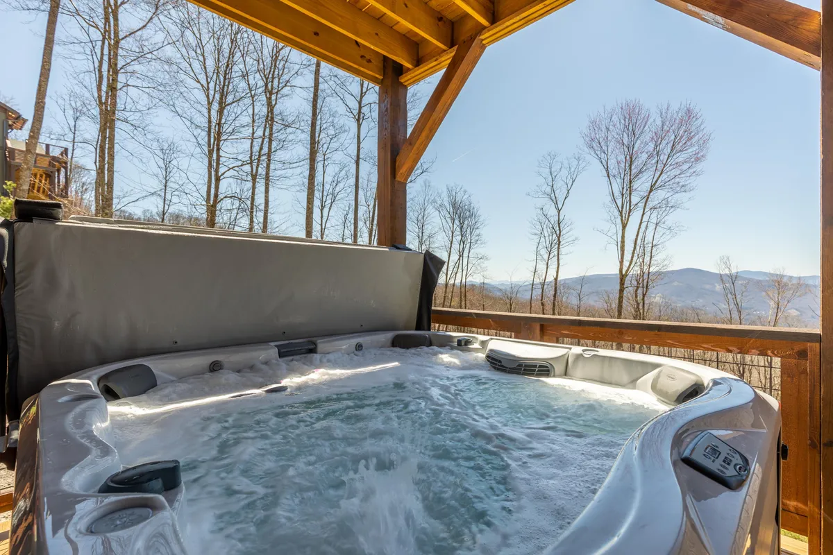 A serene exterior scene featuring a private hot tub set on a wooden deck, with sweeping mountain views in the background. The wooden structure provides a cozy, inviting atmosphere, and the setting is perfect for relaxing or socializing while soaking in the hot tub and the surrounding landscape.