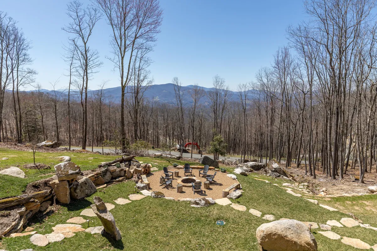 An exterior fire pit area surrounded by rustic seating and a natural stone path, all set against a stunning mountain view. The arrangement is ideal for group gatherings, storytelling, and enjoying the serenity of nature, especially under the open sky.