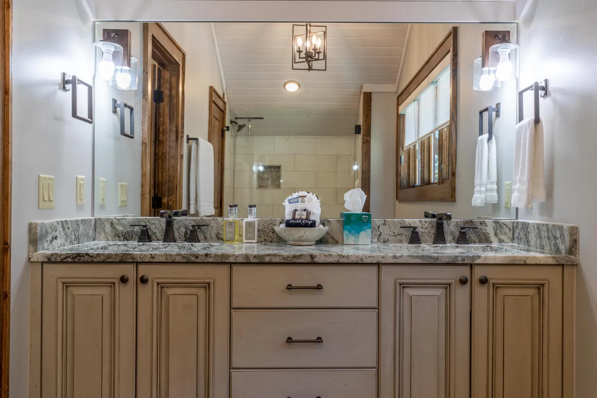 A double sink vanity in a luxurious bathroom setting, featuring granite countertops, large decorative mirrors, and modern lighting fixtures. The space feels serene and elegant, ideal for morning and evening routines.