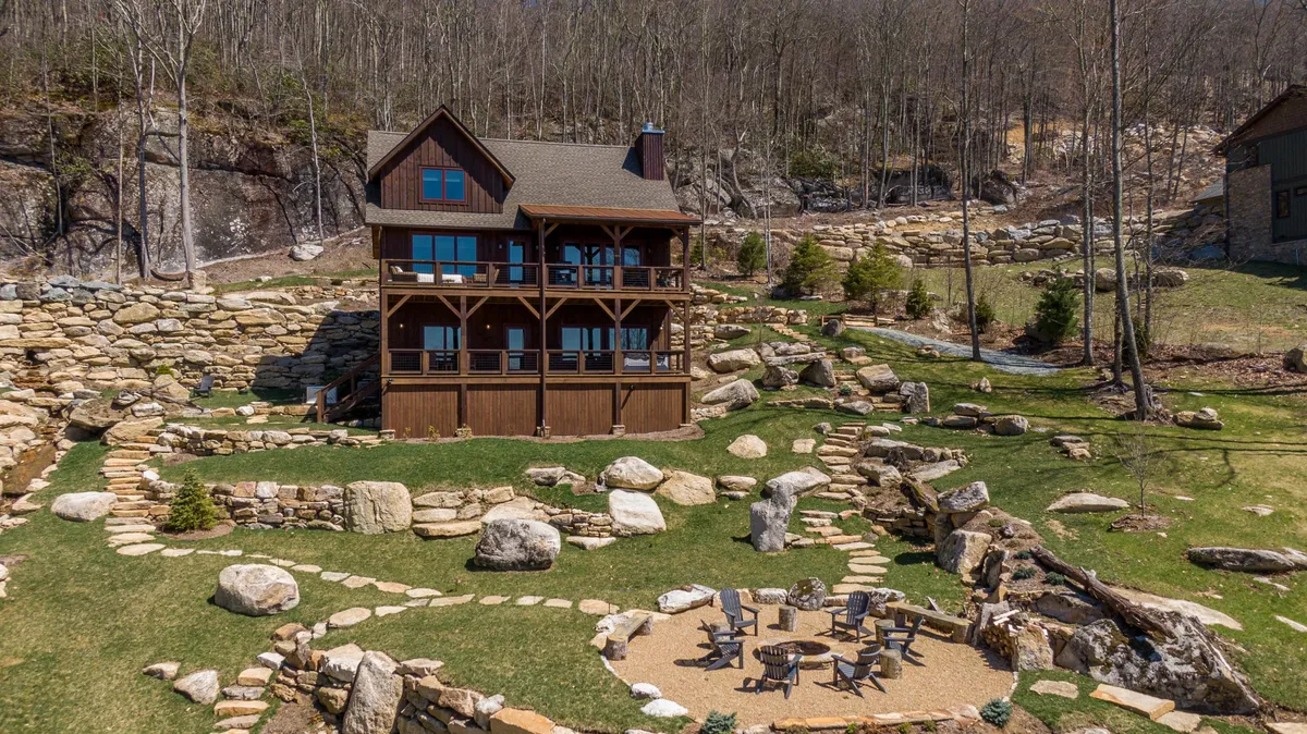 This image shows a wooden cabin nestled within a natural landscape, featuring stone pathways, an inviting fire pit area with Adirondack chairs, and lush surroundings that hint at the tranquility and togetherness found outdoors. The fire pit is an obvious focal point, perfect for group gatherings and evening storytelling under the stars.