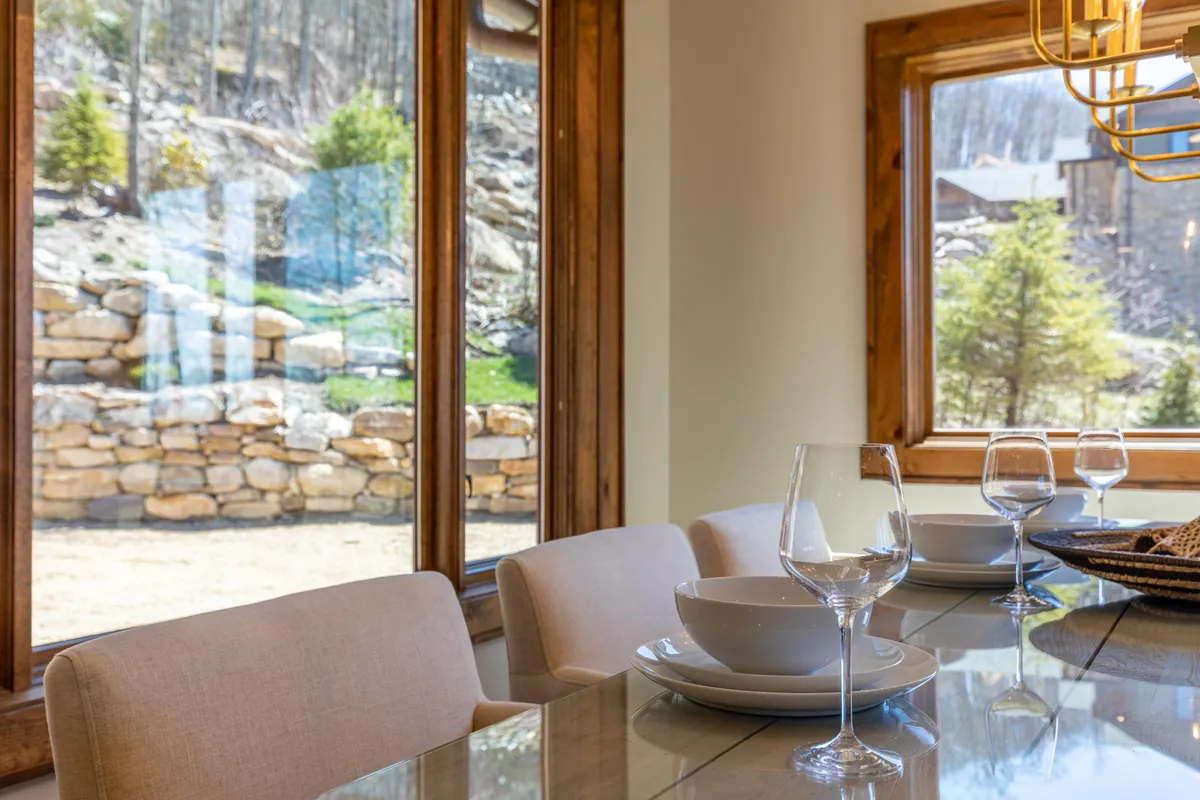 A dining table elegantly set near expansive windows that frame sweeping natural scenery. The tableware and glassware glisten in soft light, inviting family and friends to gather for memorable meals with a stunning view of the mountains beyond.